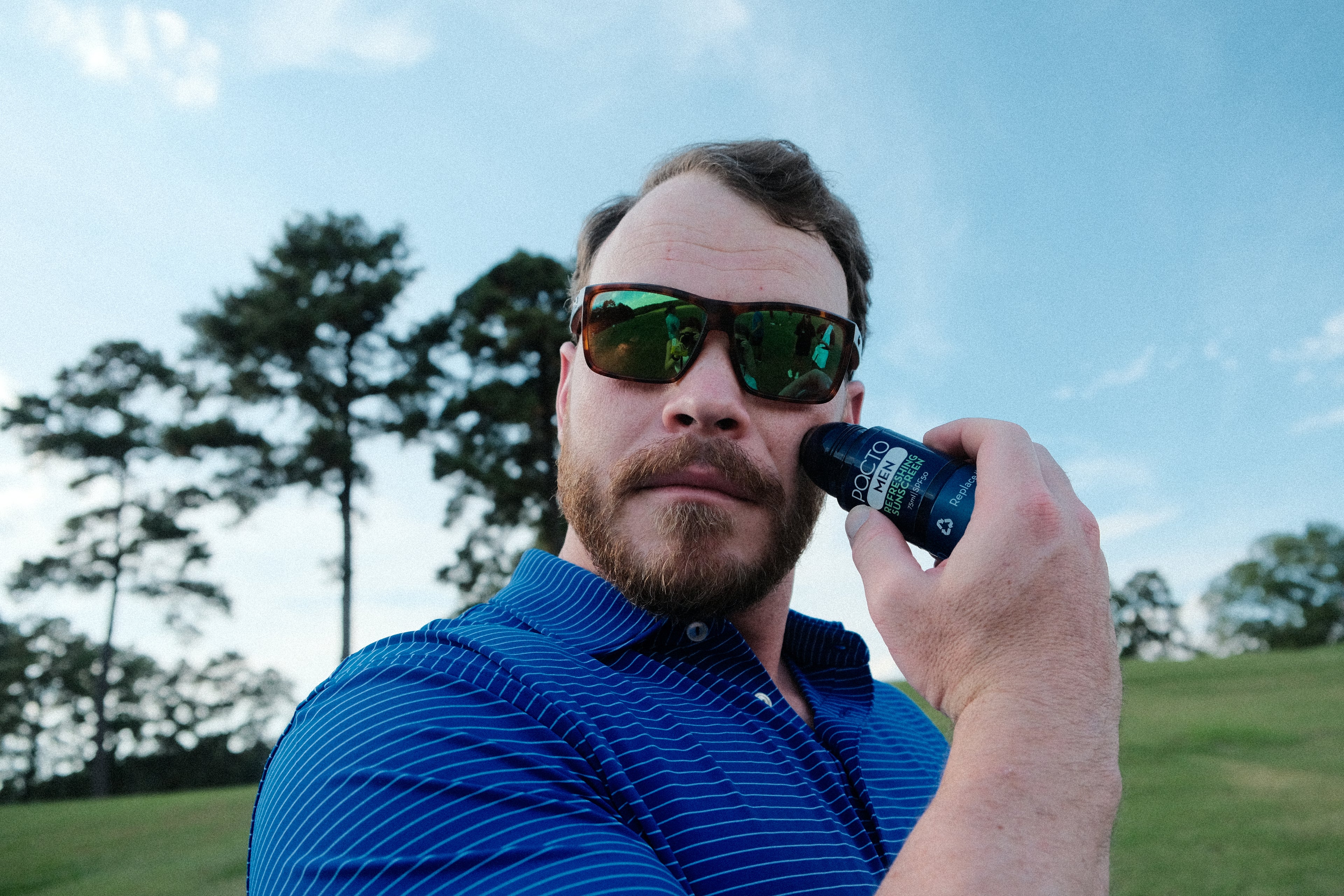Man in sunglasses holding a Pacto sunscreen on a golf course
