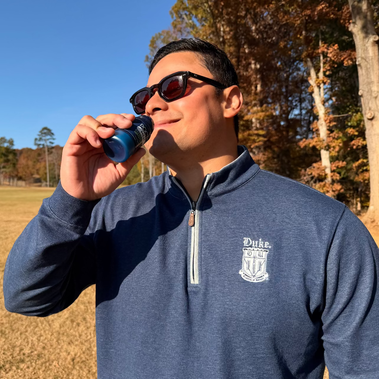 Male golfer smelling Pacto outdoors with trees and clear sky in the background