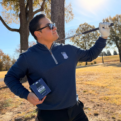 Man holding a golf club and a device in a field with trees in the background